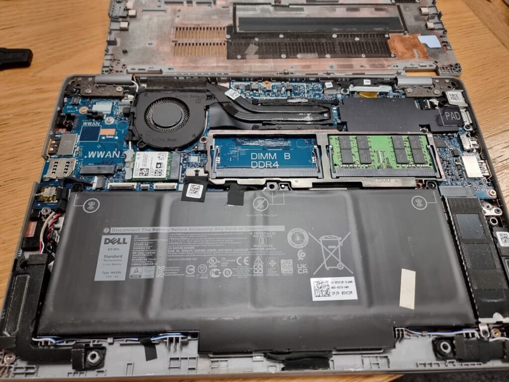Opened Dell laptop with exposed motherboard, RAM, cooling fan, and battery during professional laptop repair and hardware upgrade